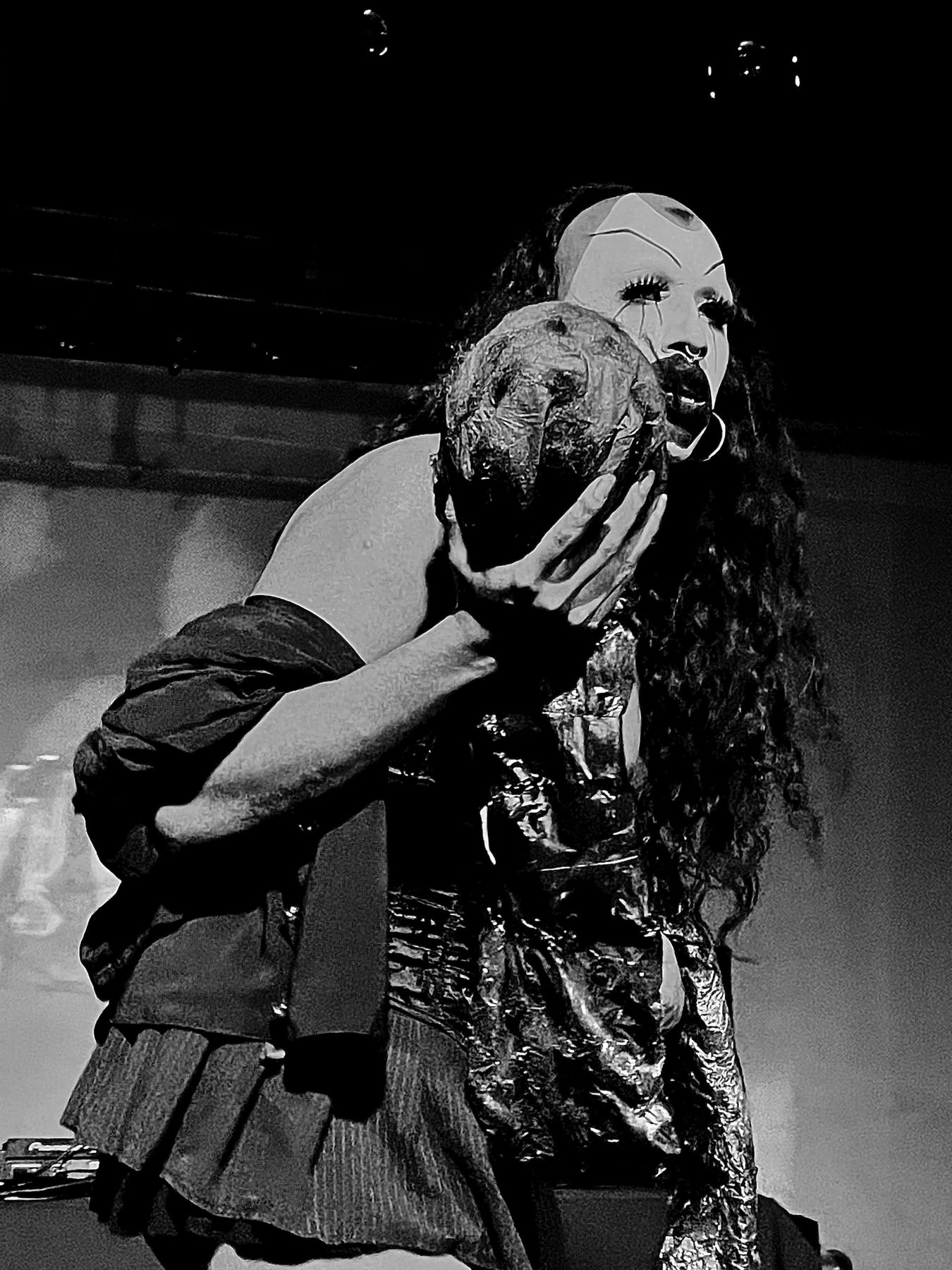 wiqi in a pale mask holding a sculpted latex head, black and white